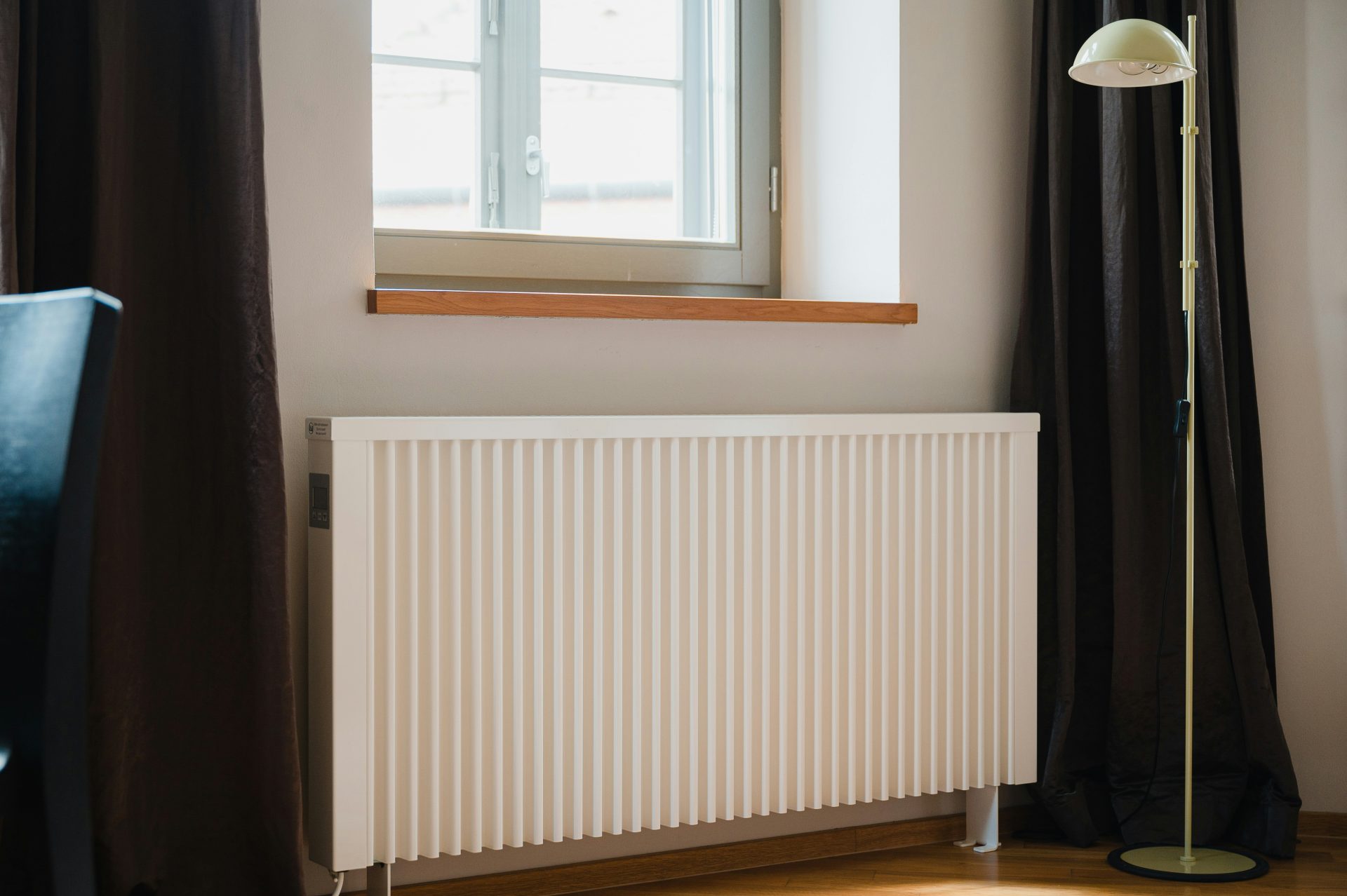 White radiator against a cream wall beneath a window that is letting in a good amount of light in the day time.