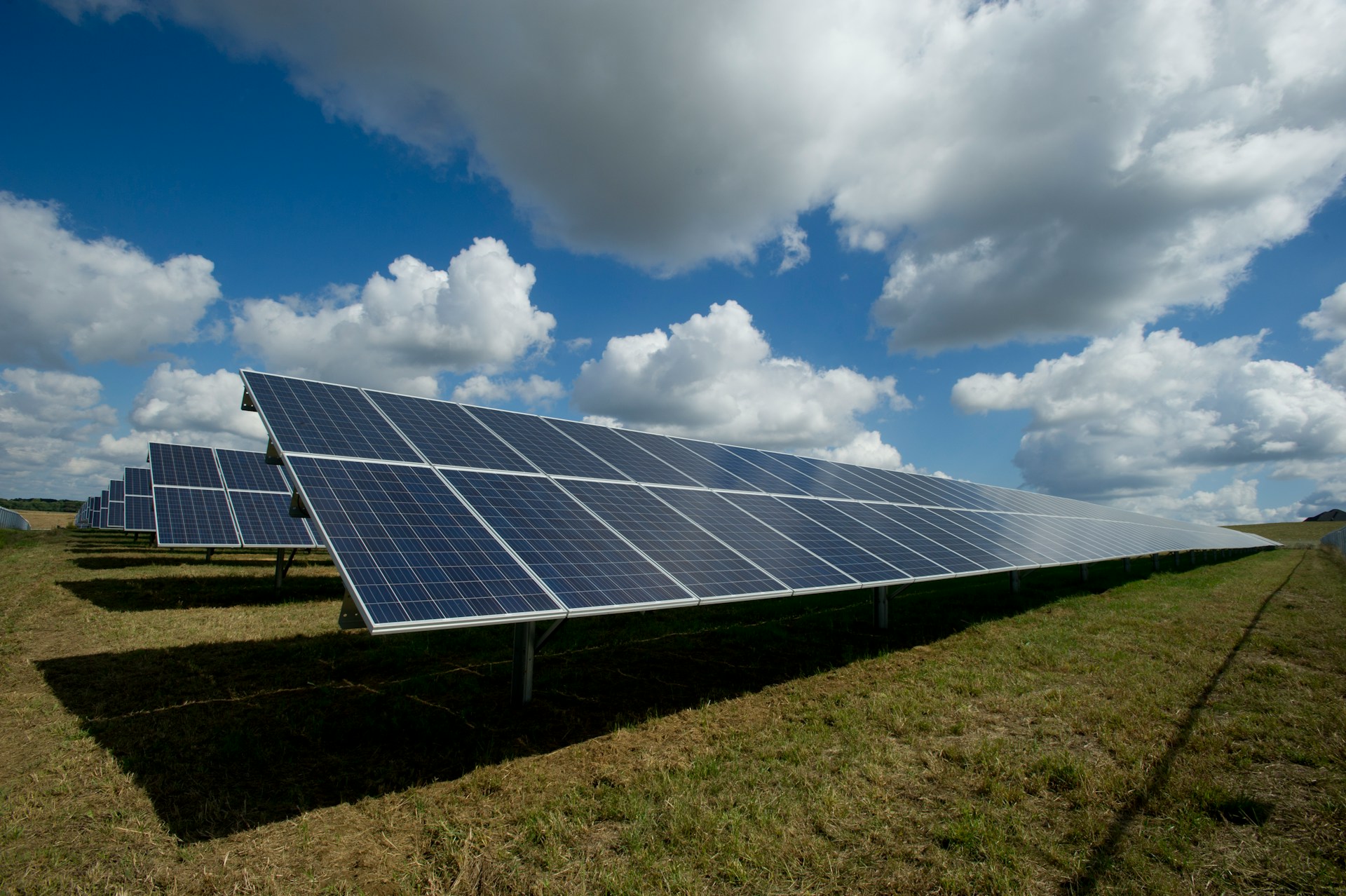 Solar panels in a field on a sunny day with some clouds above, mostly spread apart between blue sky.