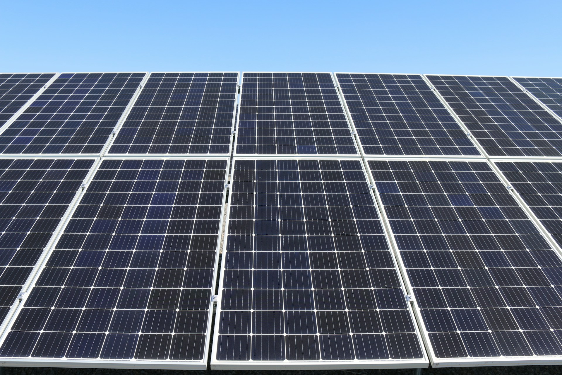 Close-up of a solar panel array, filling most of the image bar some blue sky making up the top 1/6th or so of the image.