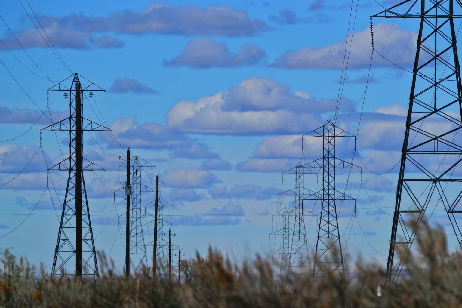 Electric transmission lines in a field on a day with some clouds against an otherwise blue sky.